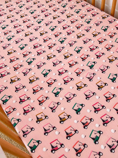 Pink fabric with a repeated pattern of colorful golf carts and small white golf balls. Ideal for playful decor.