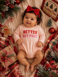 Smiling baby in a pink onesie with "Better Not Pout" text, surrounded by festive holiday decorations.