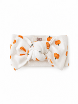 White headband with orange pumpkin print and a knot at the center, brand label visible on the back.