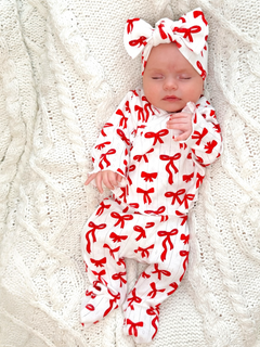 Baby girl in red and white bow-patterned pajama set, resting on a textured white blanket.