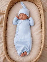 Newborn baby sleeping peacefully in a light blue ribbed outfit and hat, nestled in a cozy basket.