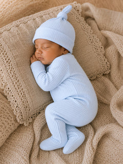 Sleepy newborn in a light blue outfit and hat, nestled on a cozy cream-colored blanket.