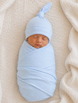 Newborn baby wrapped in light blue fabric, wearing a matching hat, resting on a textured cream blanket.