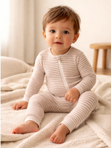 Smiling child in striped pajamas sitting on a soft blanket with a neutral background.