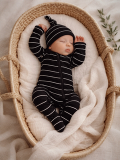 Sleeping baby in striped onesie and hat, nestled in a woven basket with soft blankets.