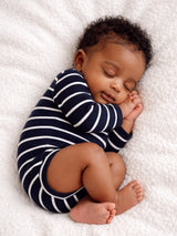 Sleeping baby in striped onesie, curled up on a soft blanket, exuding a peaceful, serene vibe.