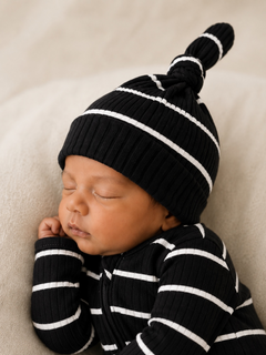 Sleeping baby in a black and white striped outfit with a matching hat, resting on a soft surface.