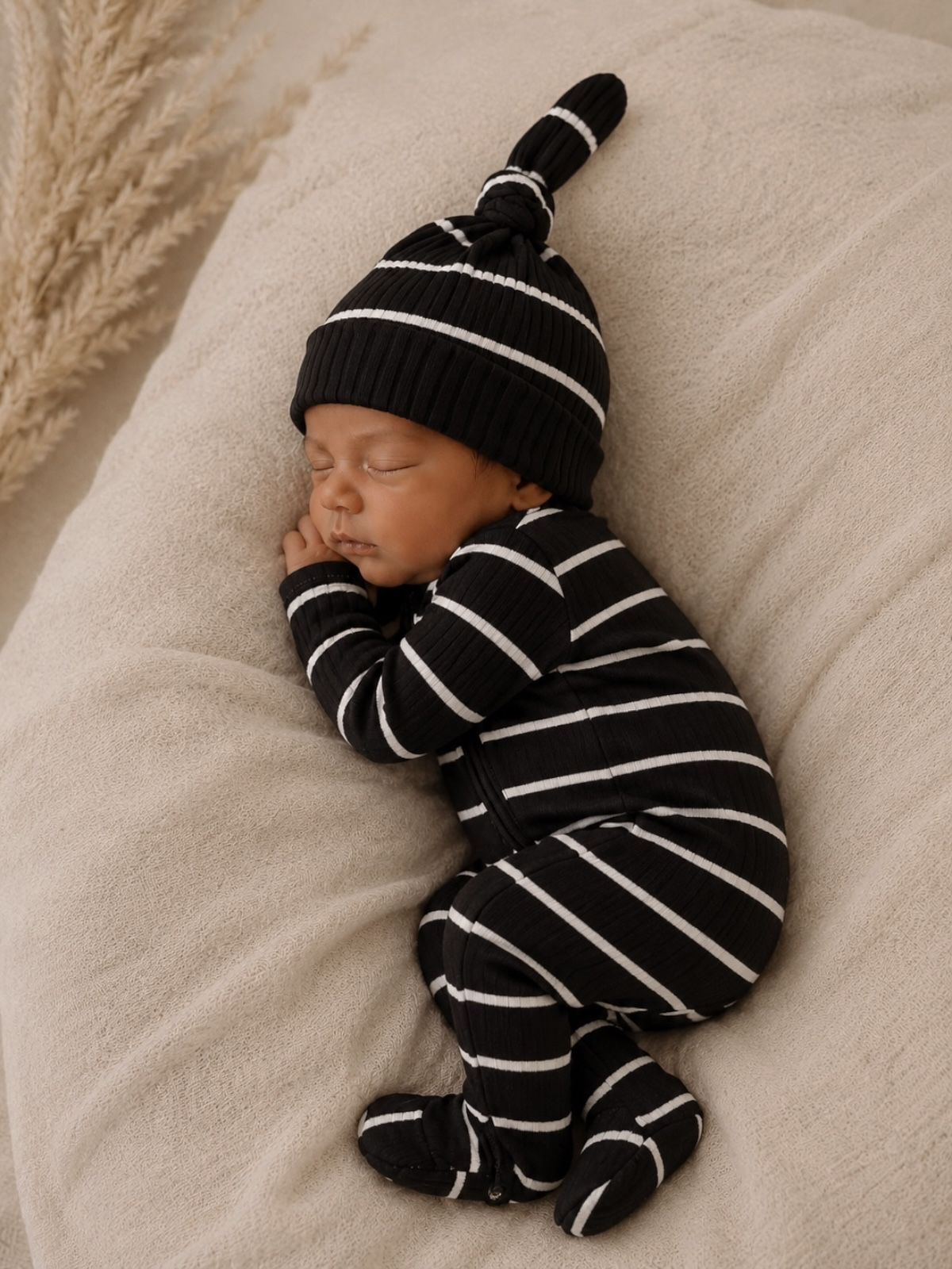 Sleeping baby in a striped black and white outfit and hat on a soft beige blanket.