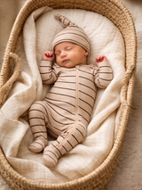 Sleeping newborn in a beige striped outfit resting peacefully in a woven basket on soft fabric.