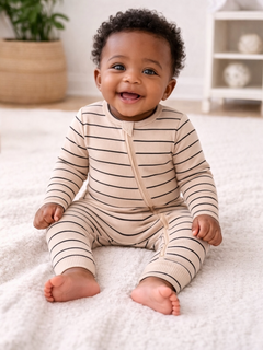 Smiling baby in striped pajamas sitting on a textured blanket. Bright and cheerful indoor setting.