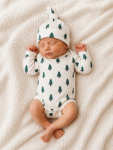 Newborn baby in a tree-patterned onesie and hat, sleeping peacefully on a textured blanket.