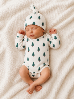 Newborn baby in a tree-patterned onesie and hat, sleeping peacefully on a textured blanket.