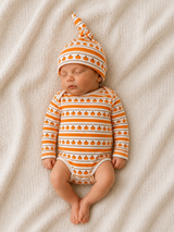Sleeping baby in striped pumpkin-patterned outfit and hat, resting on a soft blanket.