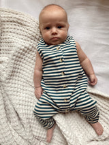Baby wearing a striped romper sits on a textured blanket, gazing directly at the camera.