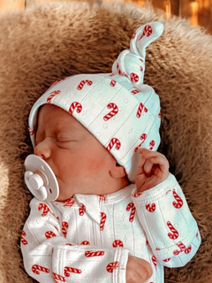 Newborn asleep in candy-cane patterned outfit and hat, with a pacifier, on a soft texture background.