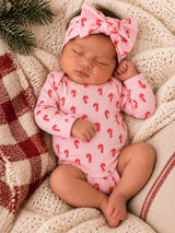 Sleeping baby in candy cane onesie with a matching headband, nestled on cozy blankets and greenery.