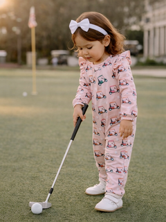 Toddler in pink golf-themed outfit practicing putting on a golf course during sunset.