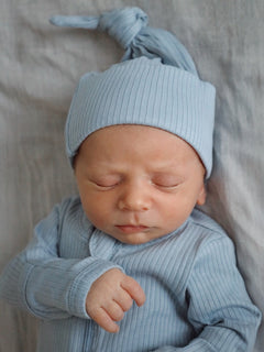 Newborn baby peacefully asleep in a light blue outfit with a matching hat, resting on a soft, neutral background.