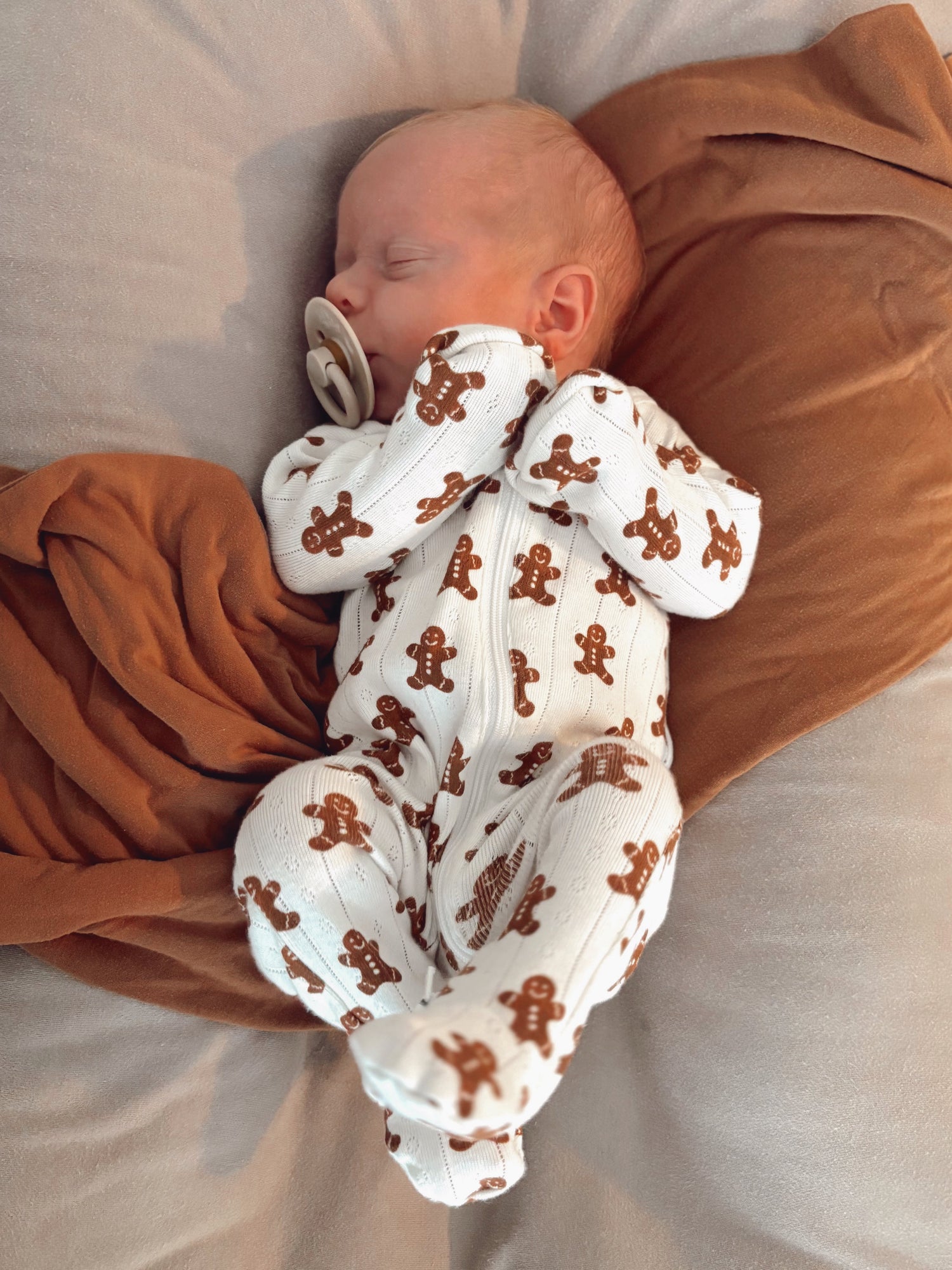 Sleeping baby in a gingerbread-patterned onesie, peacefully cradled on a soft blanket.
