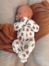 Sleeping baby in a gingerbread-patterned onesie, peacefully cradled on a soft blanket.