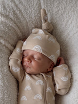 Sleeping newborn in beige rainbow-patterned outfit on a soft blanket.