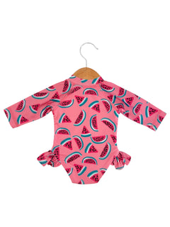Pink long-sleeve swimsuit with a watermelon pattern, featuring ruffles on the sides, hanging on a wooden hanger.