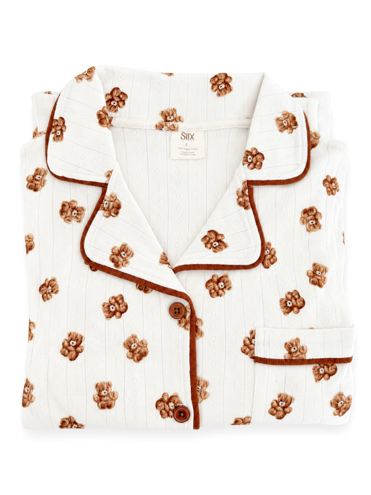 Folded white pajama set with teddy bear print and brown trim, featuring button details and a chest pocket.