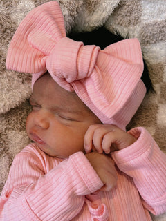 Newborn in pink outfit and oversized bow, sleeping peacefully on a soft blanket.