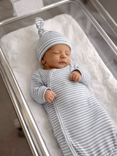 Newborn baby peacefully sleeping in a striped outfit and hat in a hospital bassinet.