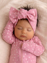 Sleeping baby girl in a pink outfit and large bow on a soft blanket.