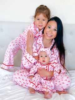 Mother and two daughters in matching pink pajamas with candy cane print, smiling together on a white bed.