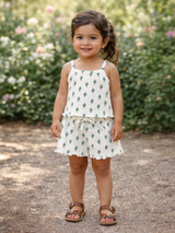 Smiling girl in cactus-pattern outfit stands on a path surrounded by greenery and flowers.