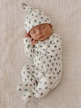 Newborn baby sleeping peacefully in cactus-patterned outfit and hat on a textured white blanket.