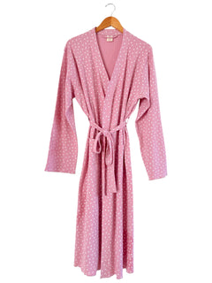 Pink robe with white polka dots, featuring long sleeves and a tied waist, displayed on a wooden hanger.