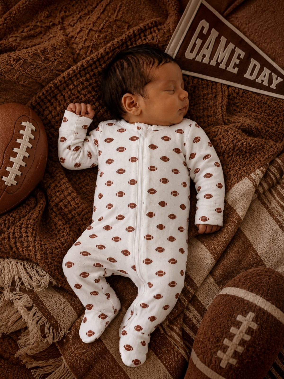Sleeping baby in a football-patterned onesie, surrounded by footballs and a 