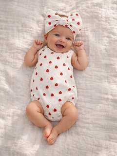 Smiling baby in a strawberry-patterned outfit and large bow, lying on a soft, textured blanket.