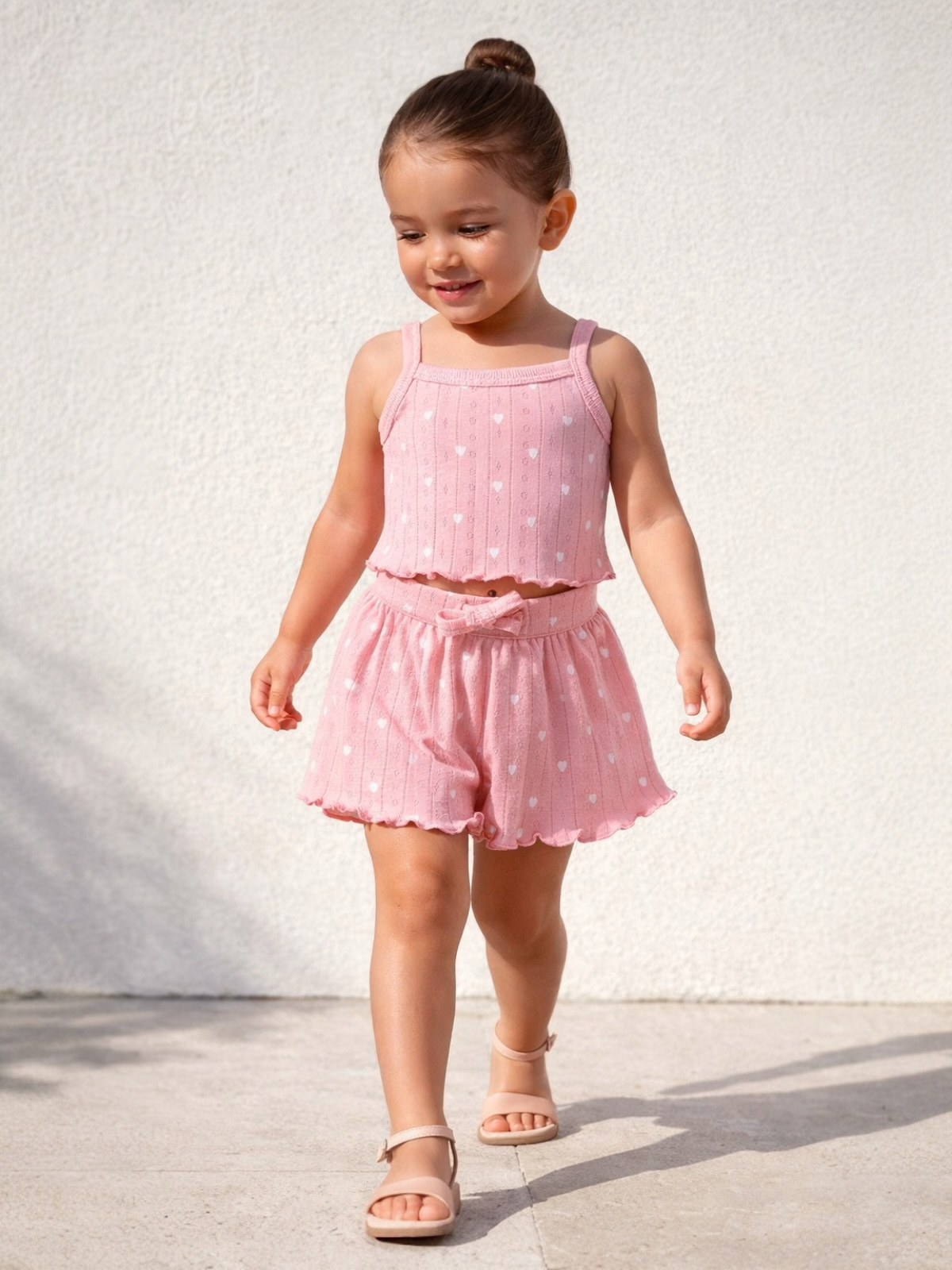 Smiling child in a pink outfit with heart patterns, walking on a light-colored surface.