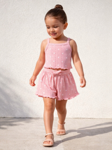 Smiling child in a pink outfit with heart patterns, walking on a light-colored surface.