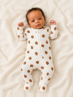 Baby lying on a soft blanket, wearing a white onesie with brown floral patterns, with arms raised in excitement.