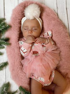 Baby girl sleeping on a pink fluffy blanket, wearing a festive outfit with a headband and tulle skirt.