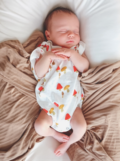 Sleeping baby in a cute mushroom-patterned onesie on a cozy blanket.