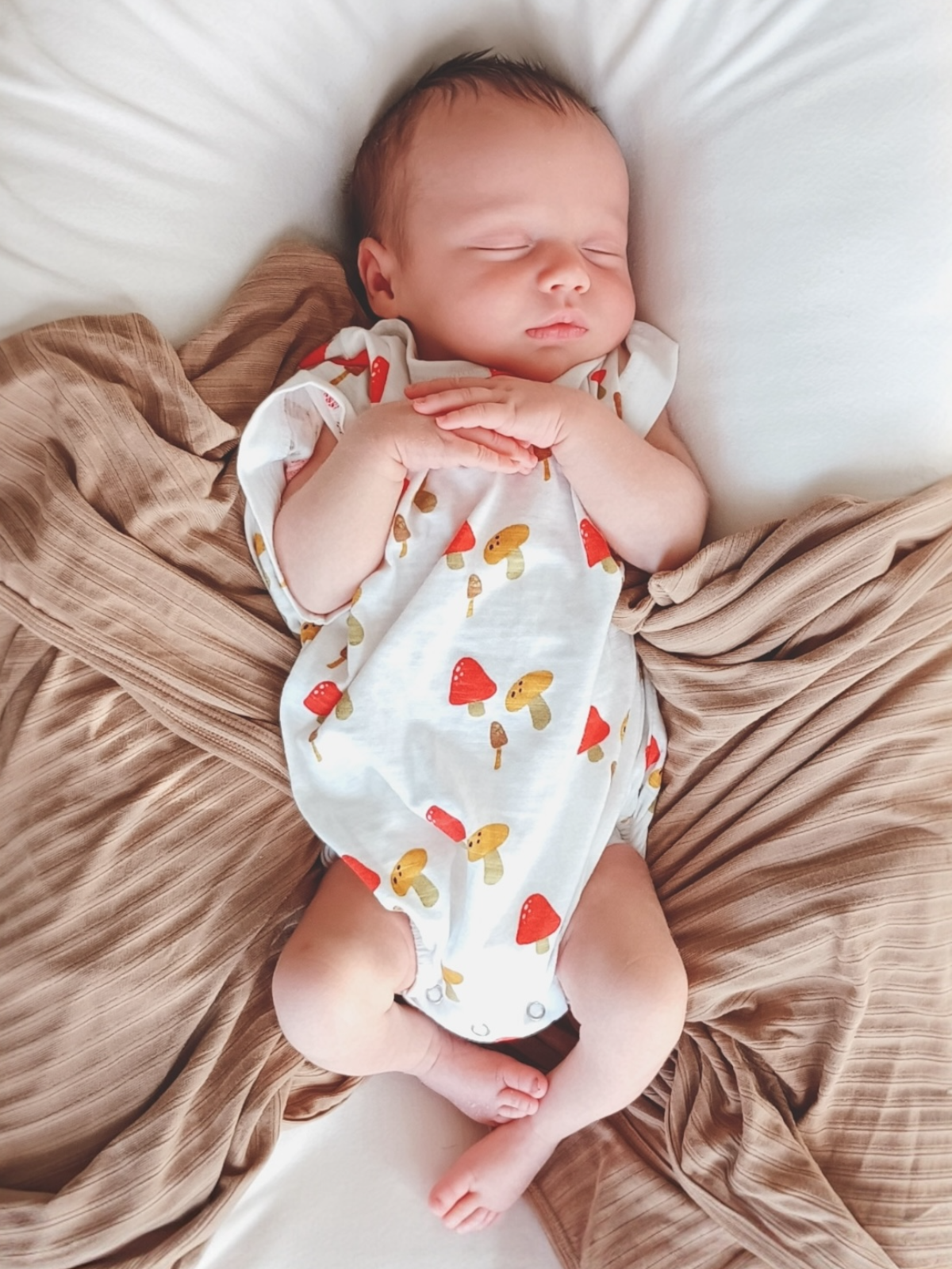 Sleeping baby in a cute mushroom-patterned onesie on a cozy blanket.