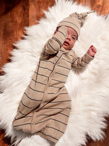 Infant wearing a striped tan outfit and hat, resting on a white fluffy rug.