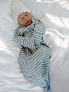Sleeping baby in striped pajamas and white hat, relaxed on a soft bed.
