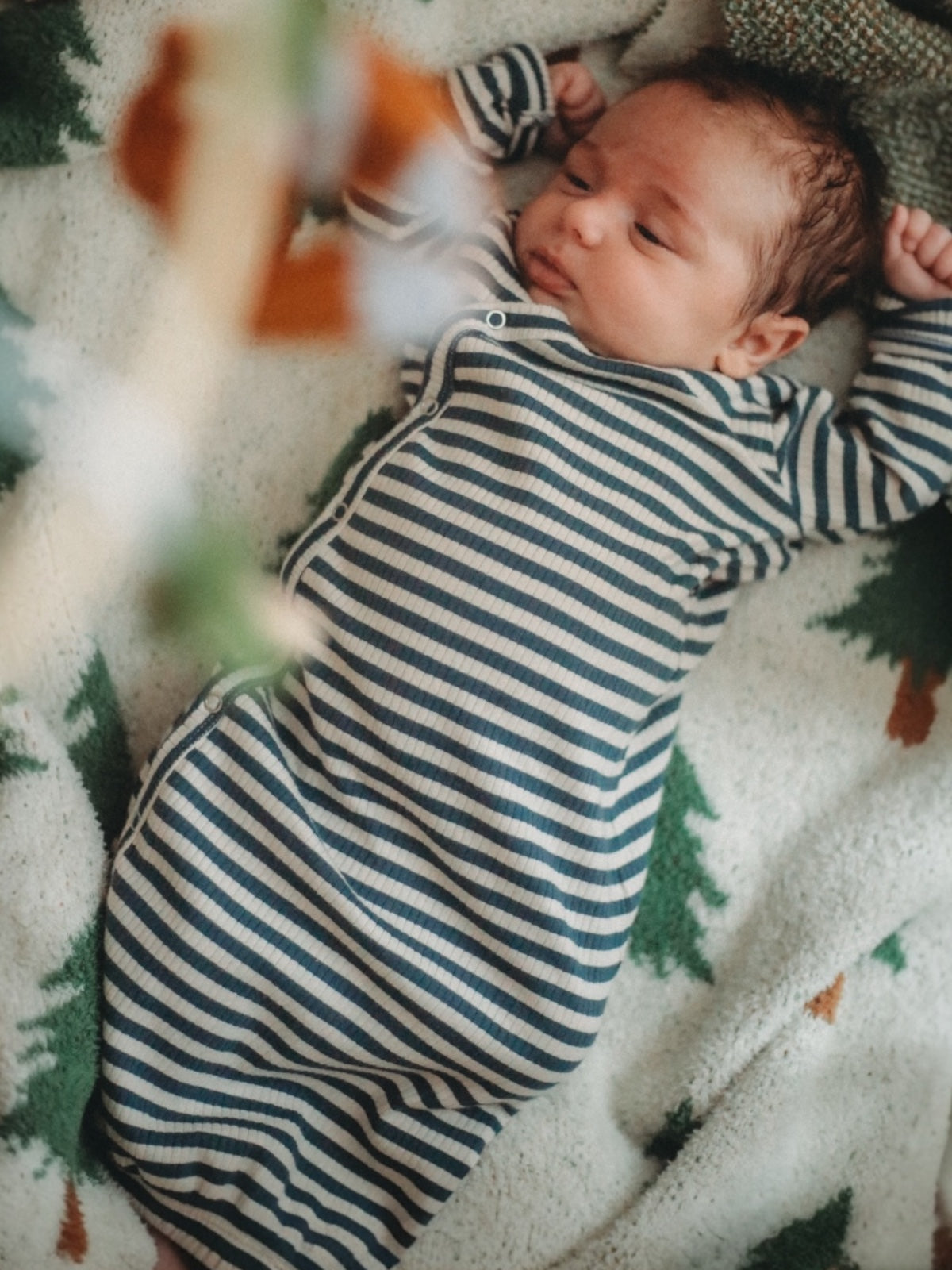 Baby in a striped onesie lying on a cozy blanket with green and orange patterns.