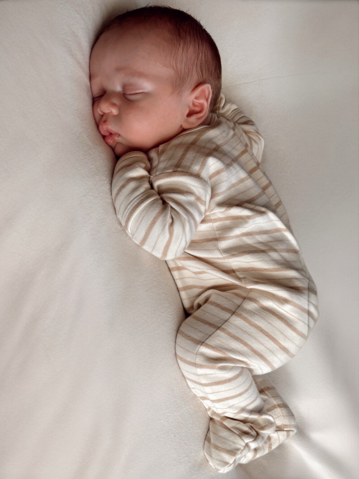 Infant sleeping peacefully on a soft surface, dressed in striped pajamas.