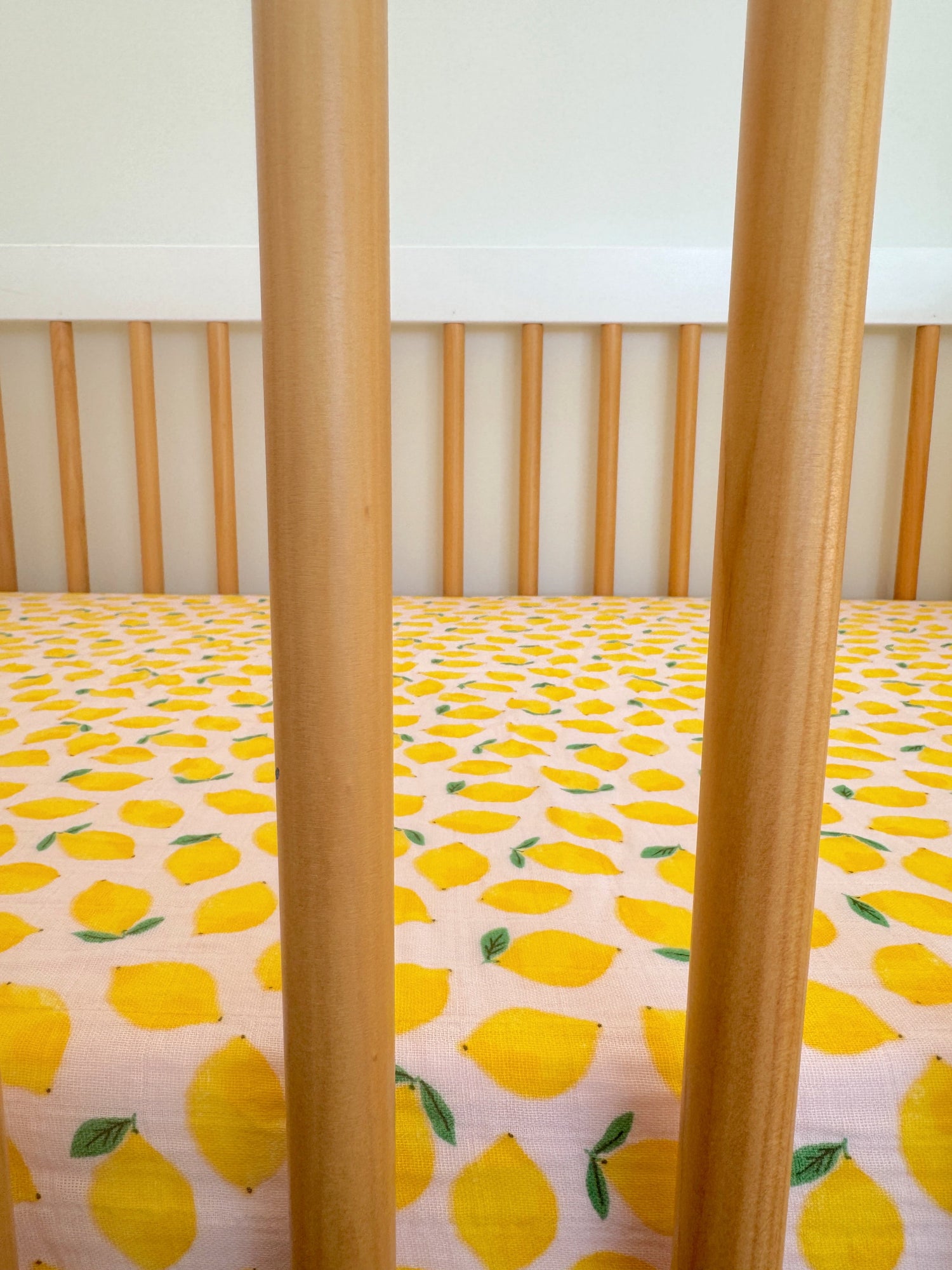 Wooden crib with vertical slats and a yellow lemon-patterned sheet.