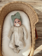 Infant in a striped onesie and green bow headband resting in a woven bassinet with a pacifier.