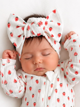 Baby girl sleeping peacefully in a strawberry-patterned outfit and large matching headband.