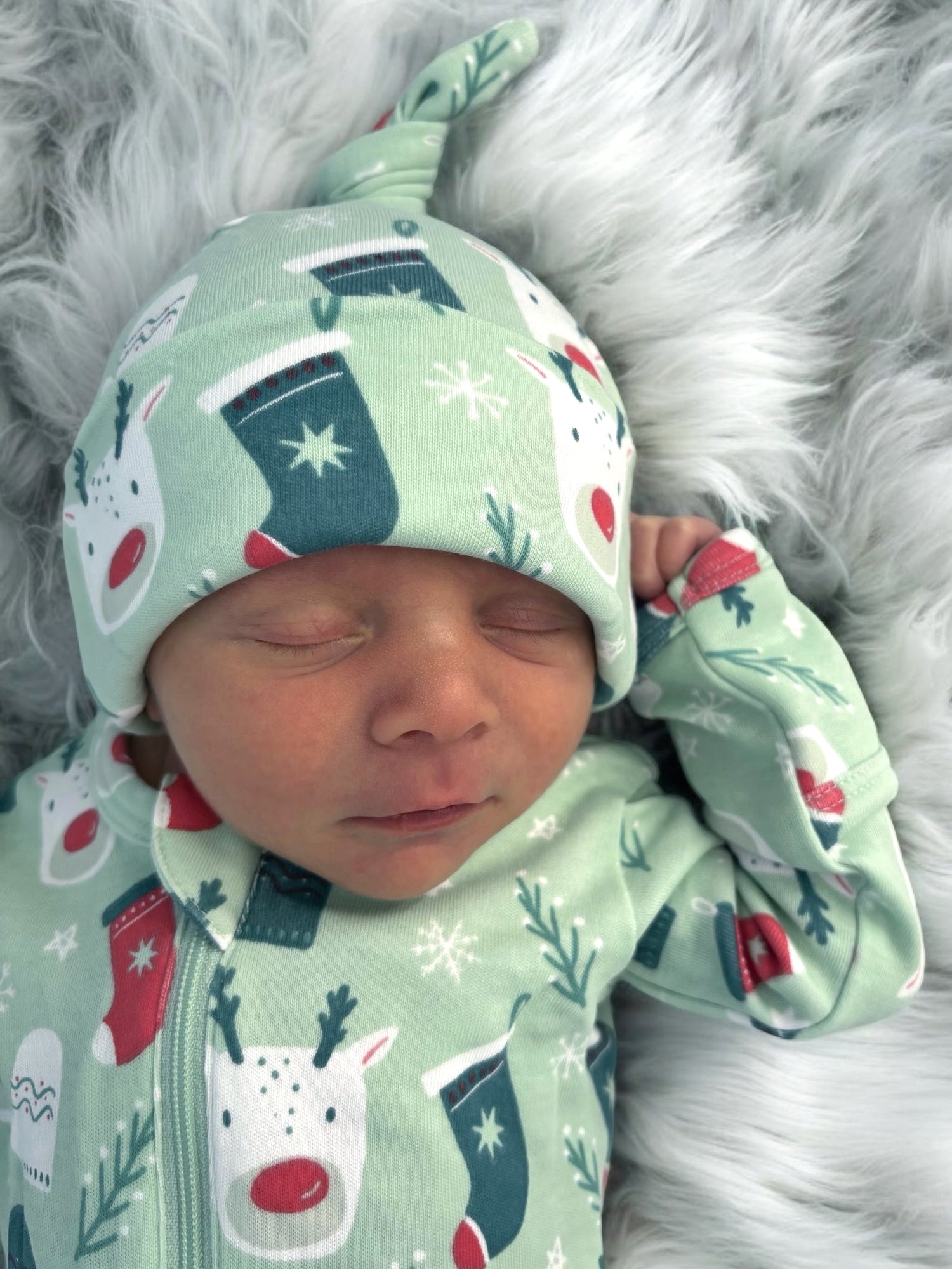 Sleeping baby in festive green outfit with holiday patterns, resting on a soft, fluffy surface.